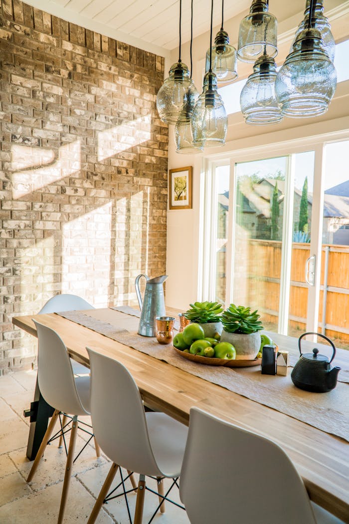 why-choose-us Sunlit dining room with contemporary decor and a rustic brick wall, featuring stylish lighting and a wooden table.
