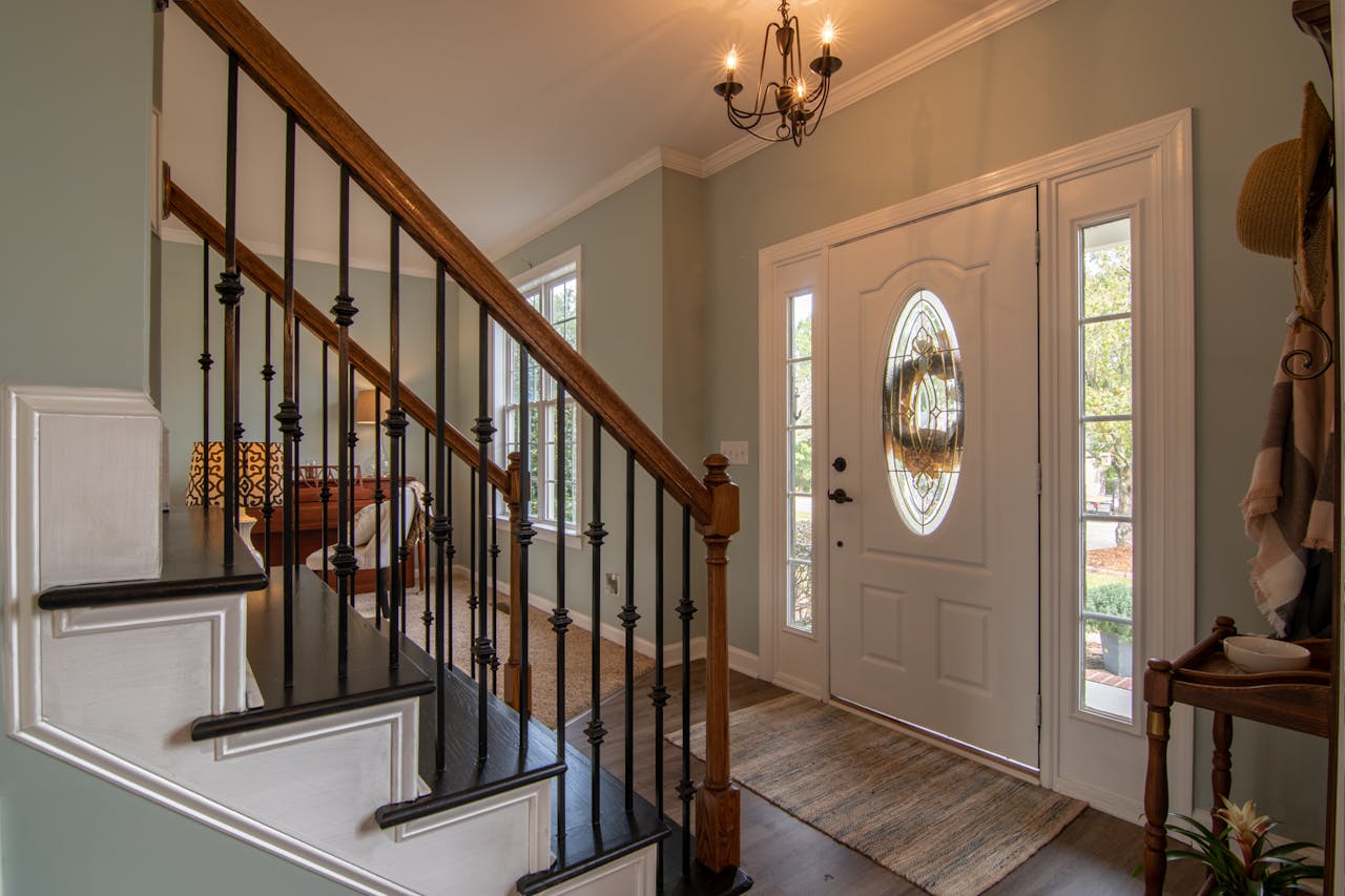 about-01 Inviting modern hallway with staircase, chandelier, and natural daylight.